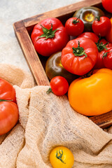 Wooden box with different fresh tomatoes on grey background, closeup