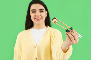 Fototapeta premium Young woman with sushi roll on green background, closeup