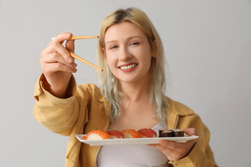 Young woman with sushi and chopsticks on light background, closeup