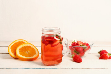 Mason jar of juice and bowl with strawberry on white wooden table