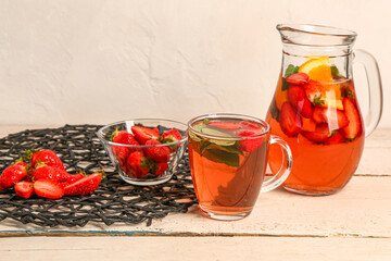 Glass and jug of tasty strawberry juice on white wooden table