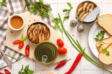 Board of canned smoked sprats and plate with bread on white tile background
