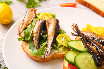 Plate of tasty sandwiches with canned smoked sprats on table, closeup