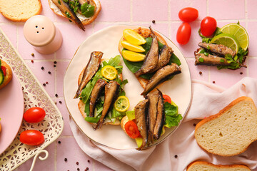 Plate of tasty sandwiches with canned smoked sprats on pink tile background