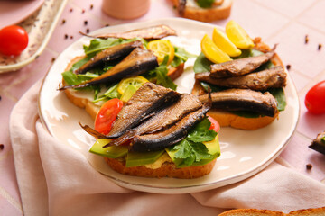 Plate of tasty sandwiches with canned smoked sprats on table