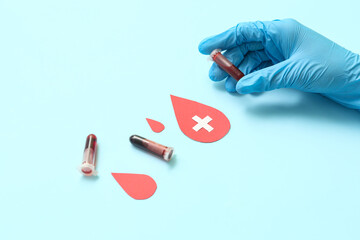 Female doctor with test tubes and paper blood drops on blue background. World Donor Day