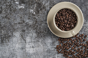 Cup of light green porcelain, full of baked coffee beans. Superior view with space for text .