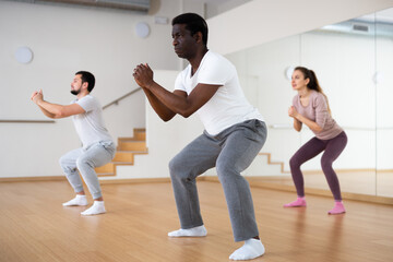 Fototapeta na wymiar Focused adult African American doing warm up before group yoga class in fitness studio