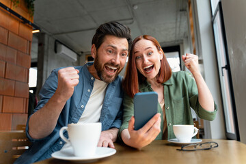 Overjoyed couple of friends holding mobile phone shopping online with sales, win money, celebration...
