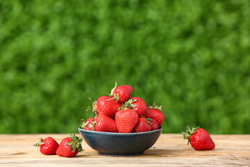 Bowl with fresh strawberry on wooden table outdoors