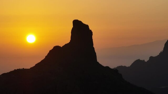 Aerial video of sunset behind Roque Bentayga on Gran Canaria with orange sky and silhouettes of Tenerife and La Gomera