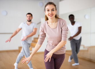 Caucasian woman dancing aerobic dance with men in studio during group training.