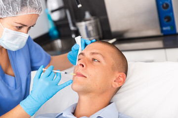 Fototapeta premium Skilled woman beautician filling males wrinkles using rejuvenating injections in clinic of aesthetic medicine
