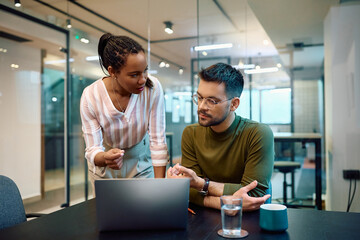 Multiracial colleagues talk while working on laptop in office.