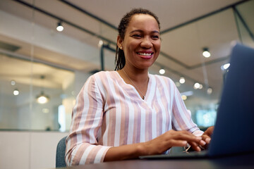 Happy black businesswoman working on computer in office and looking at camera.
