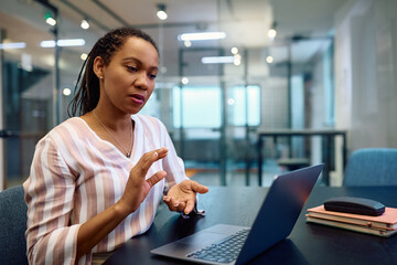 Black businesswoman talks during video call while using laptop in office.