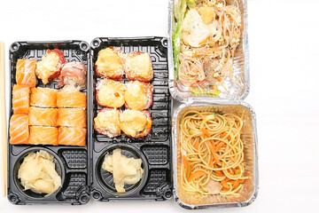 Set of fish sushi rolls with salmon,ginger,wasabi,noodles, salad packed in plastic disposable food container box on white background. Seafood, Food delivery,take out service from restaurant concept