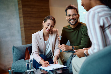 Young couple signing contract while having meeting with insurance agent in office.