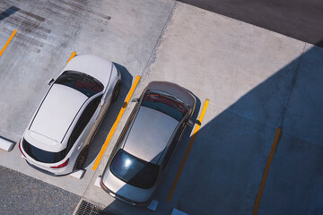 Top view of 2 cars parked on outdoor parking area in front of building with sunlight and shadow on...