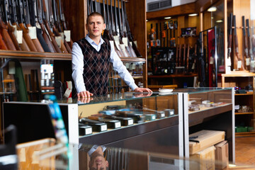 Portrait of successful confident owner of modern gun shop standing behind counter.