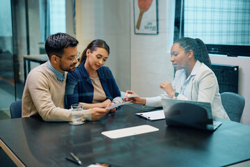 Black female financial advisor and couple going through savings plans in office.