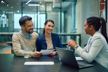 Happy couple talks about agreement with black female bank manager in office.