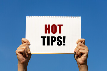 Hot tips text on notebook paper held by 2 hands with isolated blue sky background. This message can...