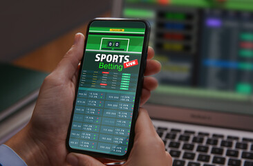 Man betting on sports using smartphone and laptop at table, closeup. Bookmaker websites on displays