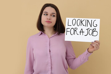 Young unemployed woman holding sign with phrase Looking For A Job on beige background