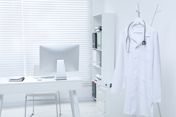 White doctor's gown and stethoscope hanging on rack in clinic