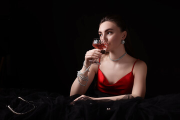 Fototapeta na wymiar Fashionable photo of attractive young woman drinking wine on black background