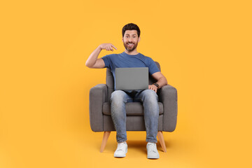 Emotional man with laptop sitting in armchair against yellow background