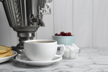 Metal samovar with cup of tea and treats on white marble table, space for text