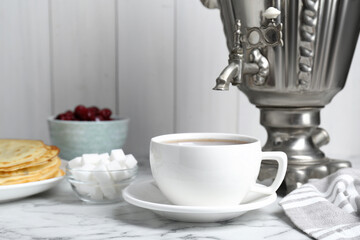 Metal samovar with cup of tea and treats on white marble table, space for text
