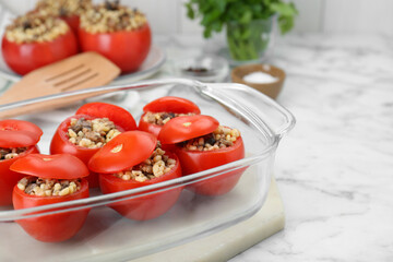 Delicious stuffed tomatoes with minced beef, bulgur and mushrooms in glass baking dish on white table. Space for text