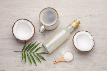 Fototapeta na wymiar Bottle of delicious syrup, halves of coconut, flakes, cup of coffee and green leaves on white wooden table, flat lay