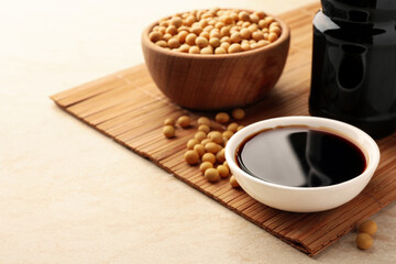 Soy sauce in bowl and soybeans on beige table, space for text