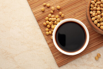 Soy sauce in bowl and soybeans on beige table, flat lay. Space for text