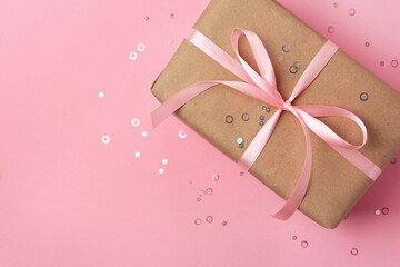 Beautiful gift box with bow and confetti on pink background, top view. Space for text
