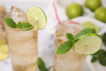Glasses of tasty ginger ale with ice cubes, lime slices and mint on blurred background, closeup