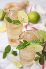 Glasses of tasty ginger ale with ice cubes, lime slices and mint on blurred background