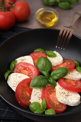 Caprese salad with tomatoes, mozzarella, basil and spices in bowl, closeup