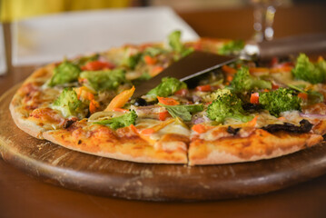 Close up of a pizza in italian restaurant. Slices of food on the wooden table. Italian cuisine in a cafe. Fresh vegan food with vegetables closeup.