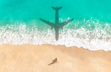 Drone view a woman sunbathing on the idyllic beach watching the shadow of an airplane fly in the turquoise blue water - Summer vacation travel concept