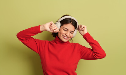 Fototapeta na wymiar Smiling young ethnic lady dancing while listening to song in headphones