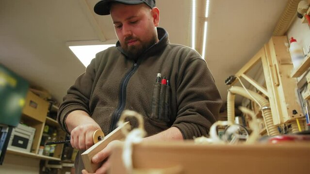 young male carpenter working on a square wooden piece surrounded by tools in the workshop. High quality 4k footage