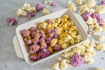 Cauliflower, white and purple, in baking pan with garlic seasoning, ready to be baked.