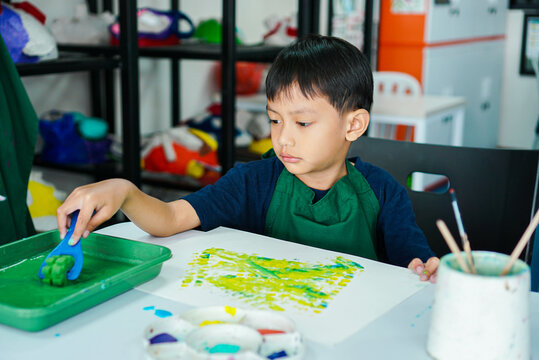 Cute little asian boy kids doing art painting activities in the classroom on the table, Indonesian, Malaysian