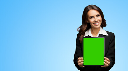 Portrait of happy smiling brunette businesswoman showing tablet pc, touchpad, with green chroma key screen, on sky blue background. Cheerful beautiful business woman at office.