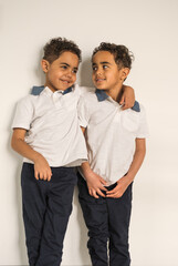 African American six year old twin boys talking to each other while leaning against white wall